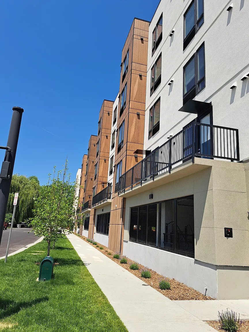 A modern apartment building with a balcony and a tree in front.
